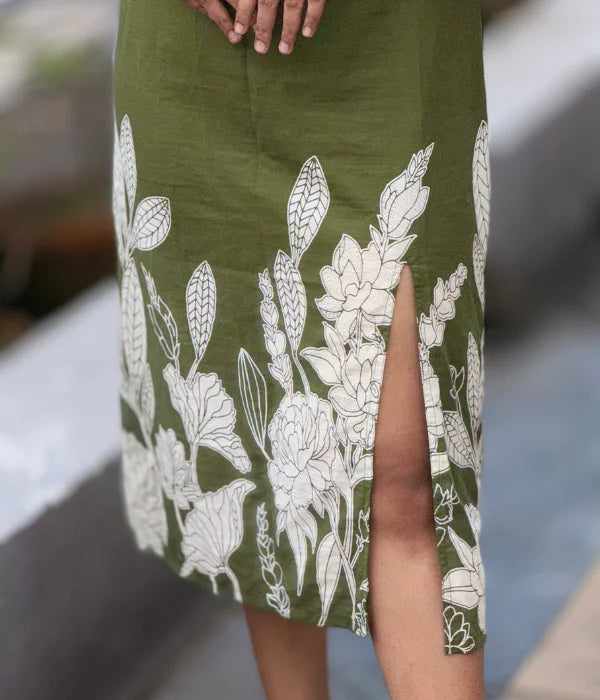 Woman in olive green cotton bodycon slit dress with hand-block leaf prints, strappy neckline, and side slit, posing outdoors. Stylish blend of ethnic and contemporary.