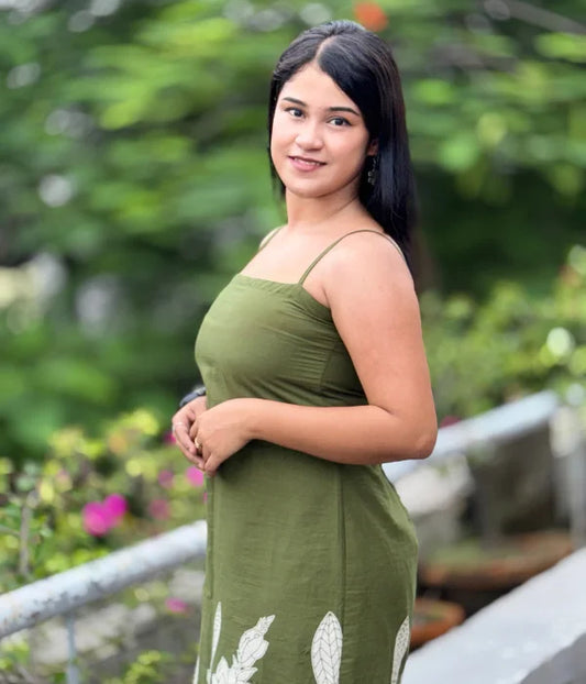 Woman in olive green cotton bodycon slit dress with hand-block leaf prints, strappy neckline, and side slit, posing outdoors. Stylish blend of ethnic and contemporary.