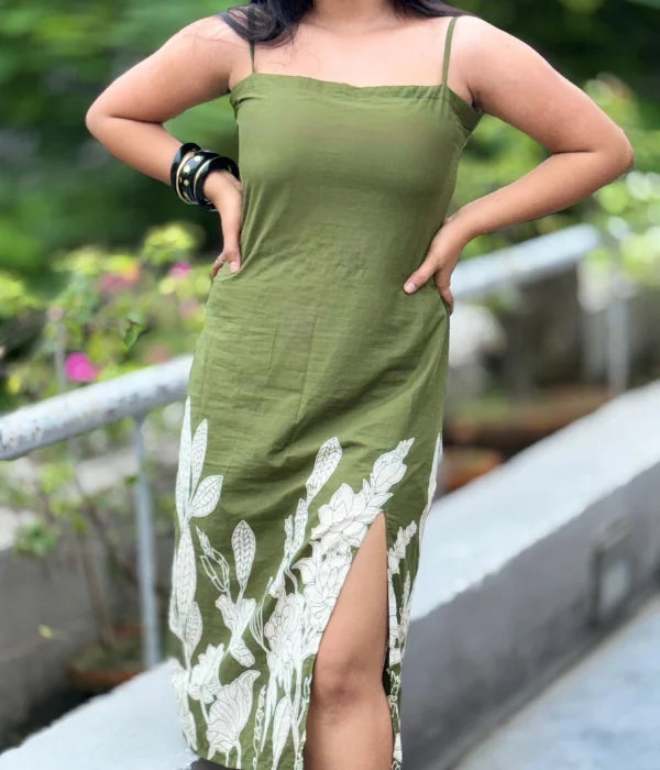 Woman in olive green cotton bodycon slit dress with hand-block leaf prints, strappy neckline, and side slit, posing outdoors. Stylish blend of ethnic and contemporary.