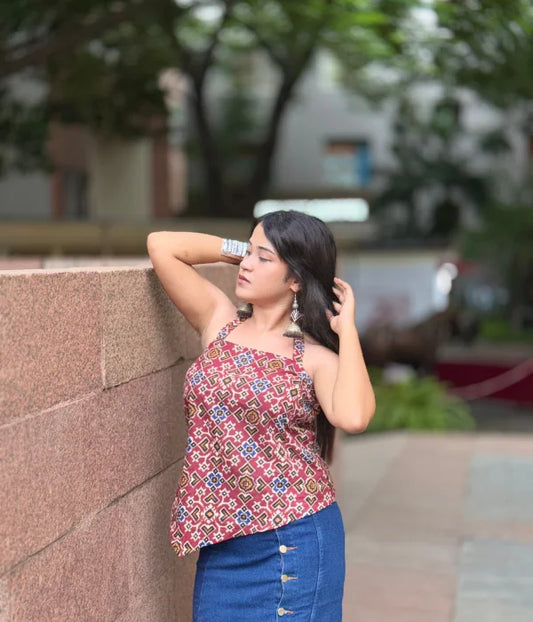 Woman wearing a bold backless halter neck top with asymmetrical hem and tie-up back, styled with blue jeans in a garden setting. Modern and breezy vibe.