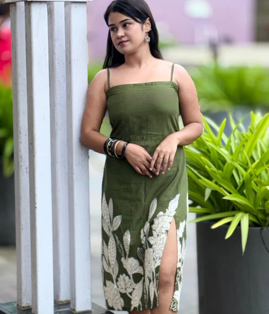 Woman in olive green cotton bodycon slit dress with hand-block leaf prints, strappy neckline, and side slit, posing outdoors. Stylish blend of ethnic and contemporary.

