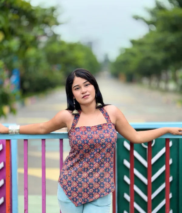 Woman posing outdoors in a stylish backless halter neck top with an asymmetrical hem, tie-up back, and shorts, surrounded by lush green plants and a poolside patio. Perfect summer fashion vibe.