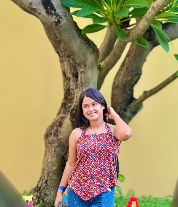 Woman wearing a bold backless halter neck top with asymmetrical hem and tie-up back, styled with blue jeans in a garden setting. Modern and breezy vibe.